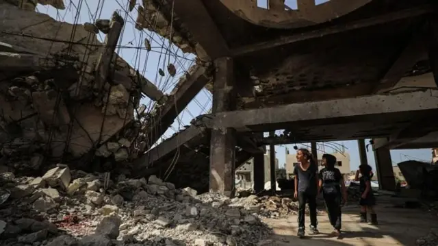 গাজায় ইসরায়েলি হামলায় ধ্বংস হয়ে যাওয়া ভবনের নিচ দিয়ে হেঁটে যাচ্ছে তিনটি শিশু 