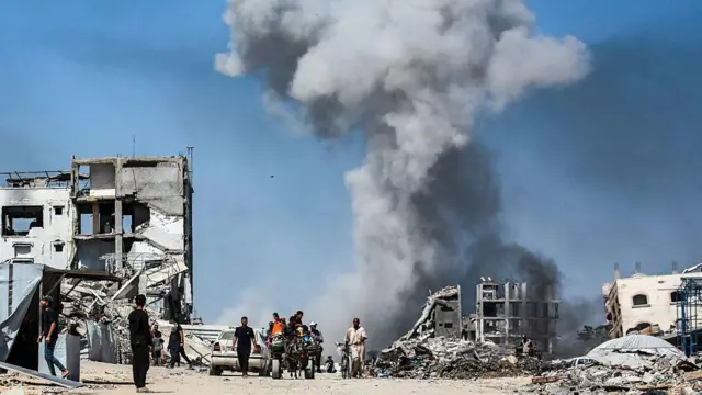 يمر الناس بجوار مبانٍ مدمرة بينما يتصاعد الدخان عقب غارة إسرائيلية على جباليا، شمال قطاع غزة، في 25 مايو/أيار 2025.