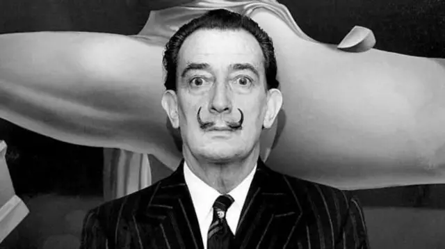 salvador dali, siyah beyaz bu fotoğrafta bir resminin önünde kameraya bakıyor