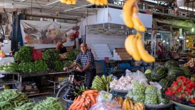 مردی ایرانی با دوچرخه از کنار مغازه های میوه و تره بار در بازاری در بوشهر، ایران، می گذرد