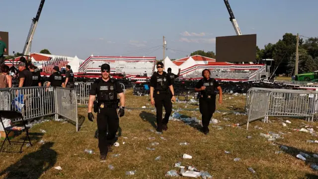 Três agentes do Serviço Secreto, vestidos com o uniforme preto, e um gramado cheioapostas presidente betcopos e embalagens plásticas. No fundo, cadeiras e uma arquibancadas vazias.