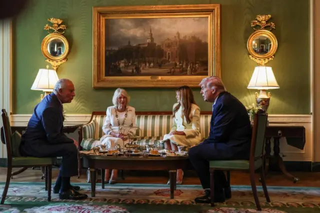 The royal couple and the Trumps, all formally dressed, talk over tea in room with green walls