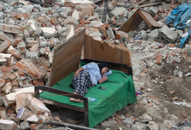 सरकारले सुकुम्बासी बस्तीमा डोजर लगाएपछि त्यहाँ बाँकी रहेको आफ्नो खाटमा सुतिरहेकी एक महिला। 