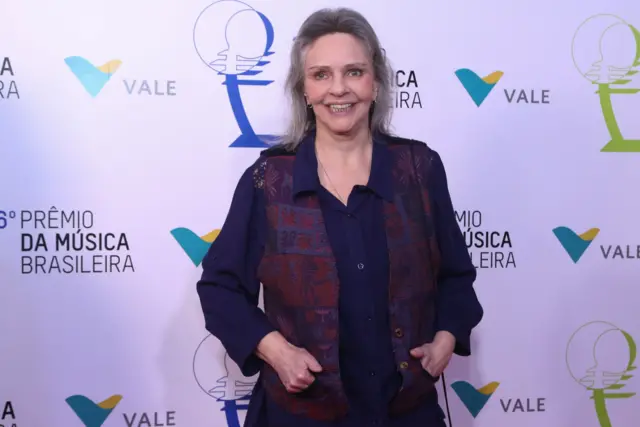 Ro Ro em frente a painel de evento, sorrindo