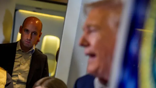 米大統領専用機の中でトランプ氏が記者団と話す様子を横からじっと見つめるミラー氏。写真ではミラー氏に焦点が合わさり、トランプ氏の顔はぼやけている