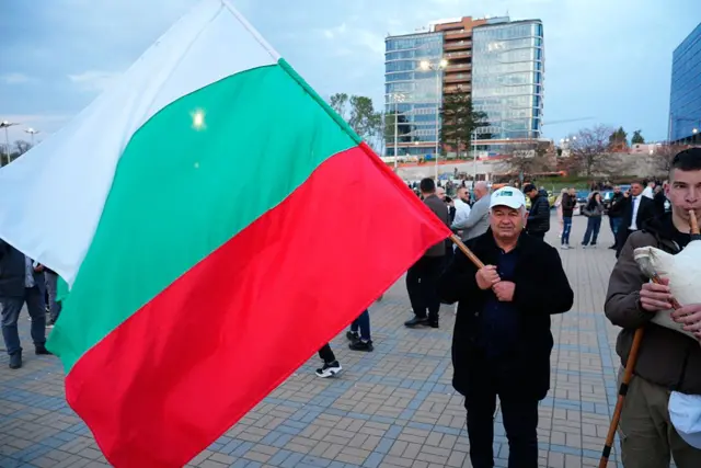 Чоловік розмахує болгарським прапором, поки люди виконують танець після мітингу партії "Прогресивна Болгарія" в Софії, Болгарія, 16 квітня 2026 року. 
