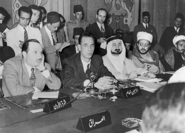أول أمين عام لجامعة الدول العربية عبد الرحمن عزام باشا خلف المايكروفون، وإلى يمينه ممثل شرق الأردن، وإلى يساره ممثل المملكة العربية السعودية خلال جلسة استثنائية لمناقشة القضية الفلسطينية في سوريا، في 19 يونيو 1946.