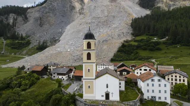 Vilarejo, incluindo igreja, com área de deslizamento atrás