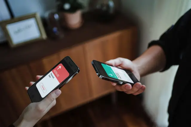 Foto recortada da mão de um homem e de uma mulher segurando um smartphone, enviando dinheiro por meio de carteira digital, usando um dispositivo de aplicativo móvel de banco on-line
