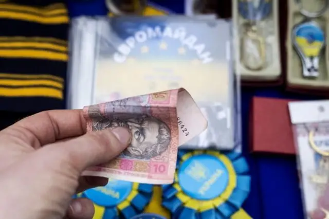 Чоловік тримає 10 грн на тлі сувенірів з Євромайдану
