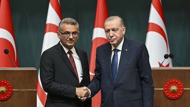 Erhürman ve Erdoğan tokalaşıyor, arkada bayraklar var