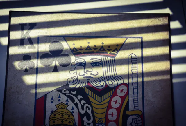 Tarjeta de rey de tréboles entre la luz y la sombra que reflejan unas rejas.