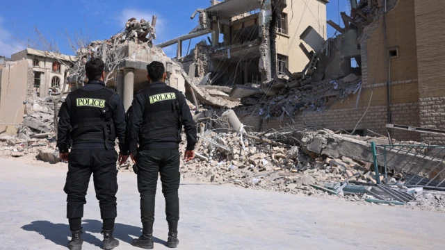 Два полицейских в форме стоят перед разрушенным зданием