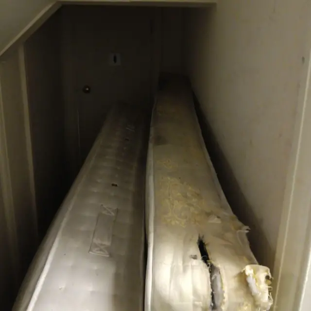 Dos colchones dañados, apilados uno junto al otro, bloqueaban una puerta. El pasillo no estaba bien iluminado.