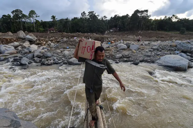 Seorang warga menyeberang jembatan darurat di Agam, Sumatra Barat pada Minggu (30/11). 