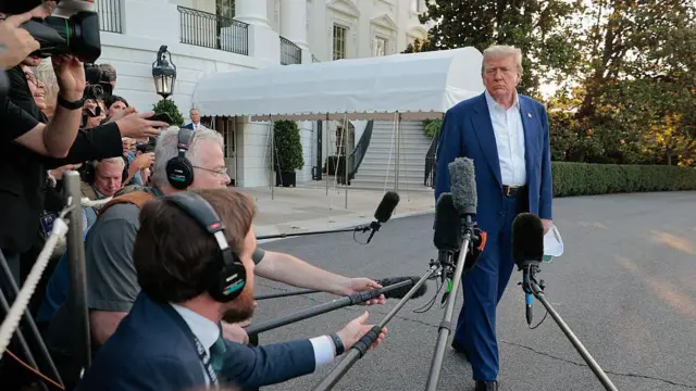 Zdjęcie pokazujące prezydenta USA Donalda Trumpa rozmawiającego z reporterami trzymającymi mikrofony i kamery, przed Białym Domem w Waszyngtonie.