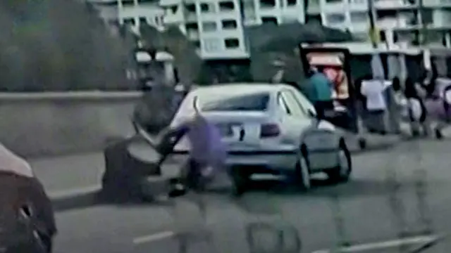 Imagen de un video granulado captado por la cámara de un auto que muestra a dos hombres forcejeando por un arma, uno vestido de negro y el otro de morado.