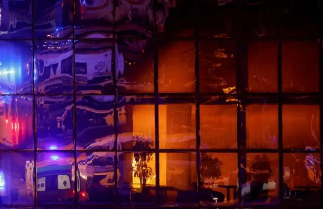 Fachada del auditorio donde se ve el reflejo de las ambulancias y el fuego