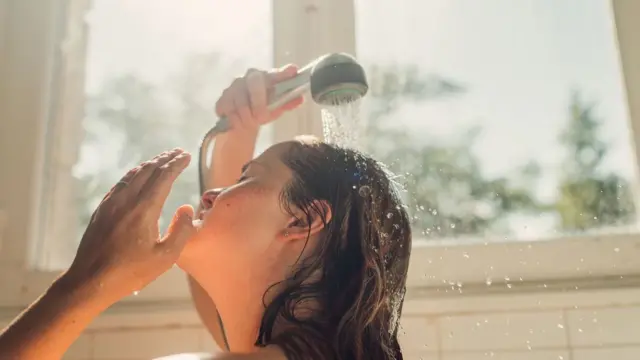 Mulher tomando banho com chuveirinho, de dia