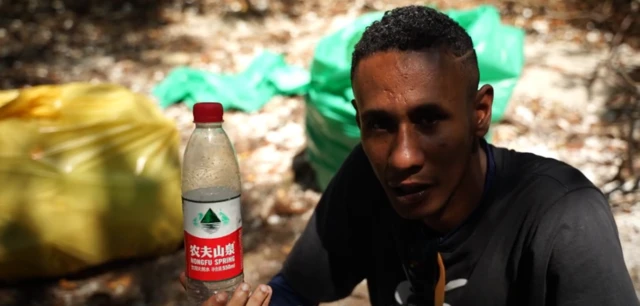 Homem segura garrafa de água com sacos plásticos ao fundo