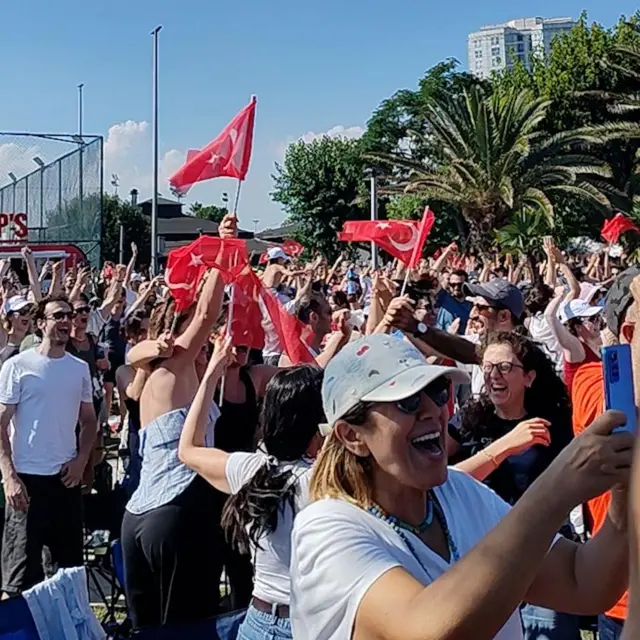  Parkta voleybol maçını izleyenler ellerinde TÜrk bayrakları ile kutlama yapıyor