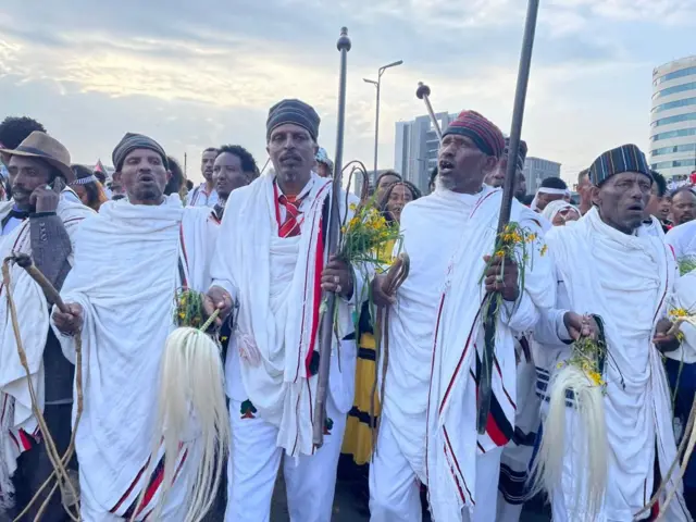 የኢሬቻ በዓልን ለማክበረ የሚወጣ ታዳሚ እንደ ሳር ወይም አበባ ያለ እርጥብ ነገር በእጁ ይይዛል