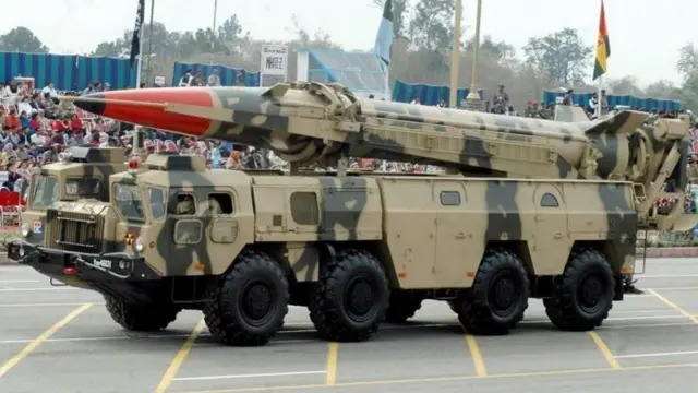 রকেট বহনকারী পাকিস্তানের একটি সামরিক যান যার ওপরে তিনটি পতাকা লাগানো আছে, প্রদর্শনী দেখছেন অনের বেসামরিক মানুষ 