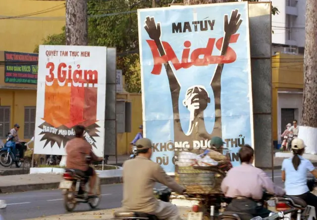 People ride past posters depicting drug addiction as one of three main social issues that Ho Chi Minh-City is facing in Ho Chi Minh, 16 January 2003. 