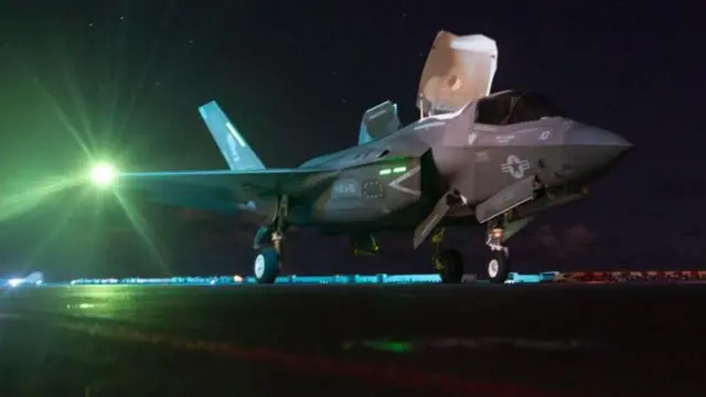 Um caça F-35 americano em um porta-aviões sob um céu noturno