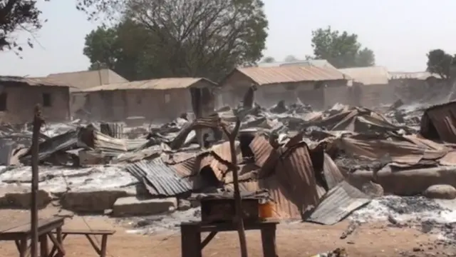Burnt wooden stalls and corrugated iron from one market for di aftermath of di attack.