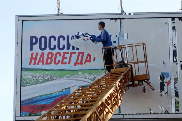 Рабочий обдирает плакат “Россия навсегда” после освобождения Херсона украинскими войсками