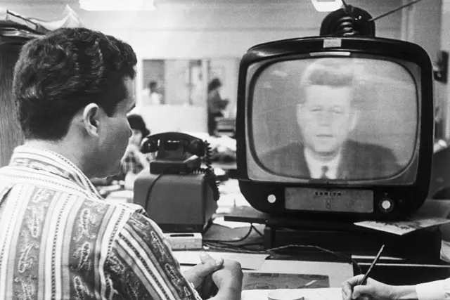 Homem assistindo a TV onde aparece John F. Kennedy fazendo pronunciamento