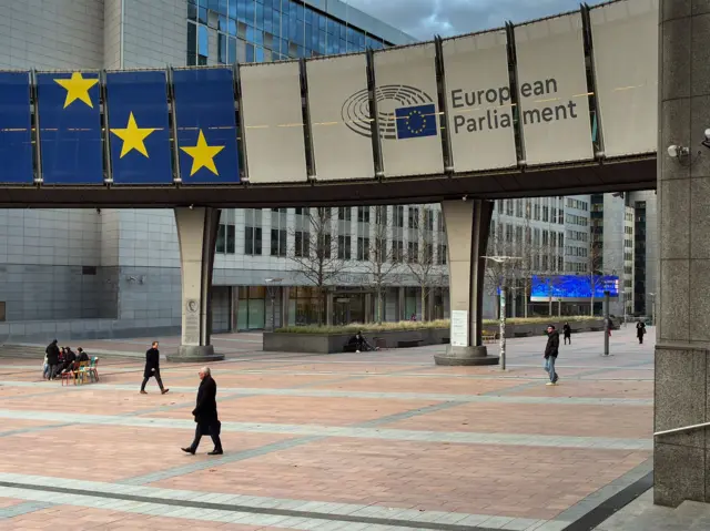 Площадь, окруженная зданиями. По площади ходят люди. На одной из построек надпись European parliement.