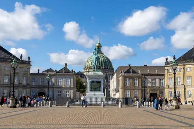 Foto de uma praça em Copenhague com pessoas em volta e uma estátua no fundo