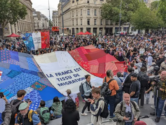 Aşırı sağ karşıtı göstericiler "Fransa'nın kumaşı göçle dokunmuştur" yazan bir bayrak taşıyor