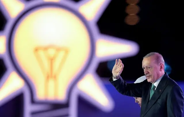 Cumhurbaşkanı Erdoğan, sahnede el sallıyor. Arkasında AKP logosu var. 