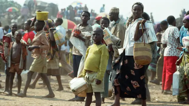 Deca i odrasli napolju stoje u masi i drže činije za hranu i svoje stvari
