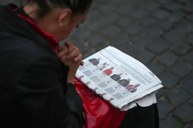 gazetedeki potansiyel papa adaylarına bakan bir kadın