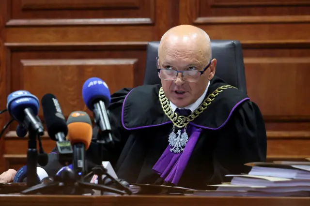 Мужчина в очках и судейской мантии за столом с микрофонами