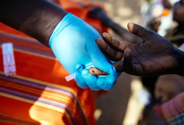 L'image montre un professionnel de la santé portant un gant bleu en train de prélever une petite quantité de sang sur le doigt d'une autre personne pour un test de dépistage rapide.
