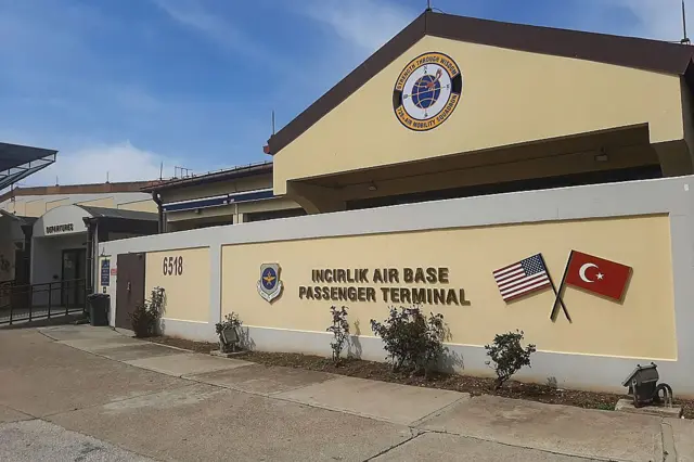 Bir binanın sarı duvarında İncirlik Hava Yolcu Terminali yazıyor. Yanında Türk ve Amerikan bayrakları var