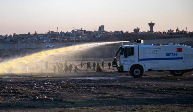 Bir TOMA aracından sarı renkli bir sıvı göstericilere doğu sıkılıyor. Arkada Nusaybin ilçesi evleri görülüyor.