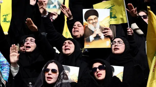 سيدات بلباس أسود، يشاركن في مراسم تشييع حسن نصر الله، يحملن صورته وأعلام حزب الله الصفراء.