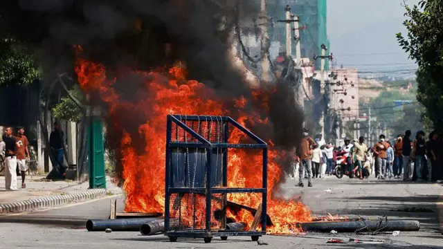 Llamas rojas brillantes arden en la calle mientras la gente se reúne a lo lejos, el 8 de septiembre de 2025.