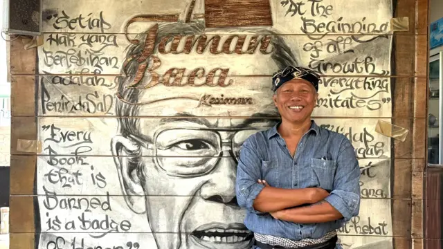 Agung Alit berfoto di depan lukisan wajah Pramoedya Ananta Toer yang ada di Taman Baca Kesiman.