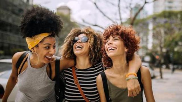 Três amigas sorrindo e abraçadas caminhando na rua