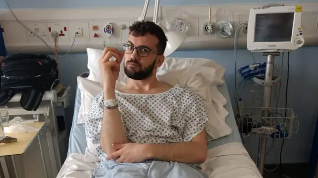 Chris leży w szpitalnym łóżku trzymając w dłoni orzeszek ziemny przed jego zjedzeniem, podczas badania klinicznego na odczulanie osób z alergią na orzeszki ziemne