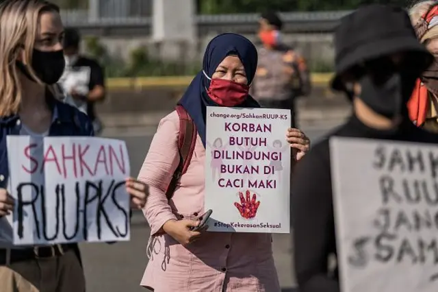 Aktivis perempuan Indonesia mengenakan masker wajah sambil memegang plakat, saat demonstrasi di depan di Dewan Perwakilan Rakyat Indonesia (DPR) untuk segera meloloskan Rancangan Undang-Undang Penghapusan Kekerasan Seksual (PKS) di Jakarta, Indonesia, Selasa, 7 Juli 2020. 