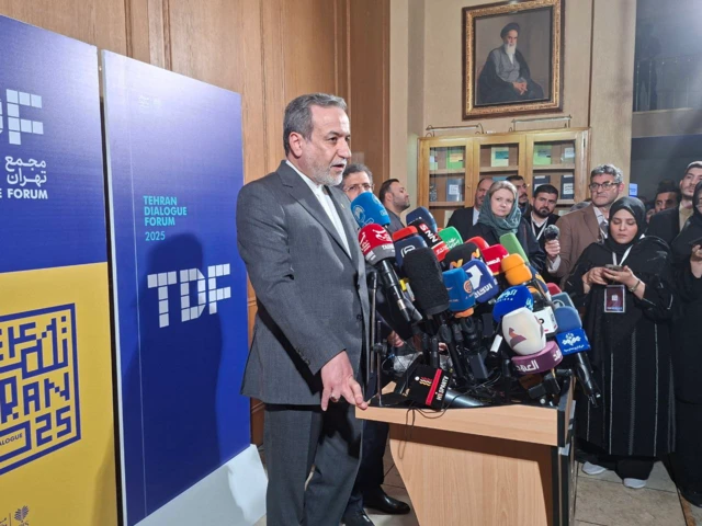 عباس عراقچی، وزیر خارجه ایران، در یک سالن کنفرانس دیده می‌شود که به سئوالات خبرنگاران پاسخ می‌دهد. روی میز خطابه پیش روی او شمار زیادی از مایک‌های رسانه‌ّای داخلی بو بین‌المللی دیده می‌شود.