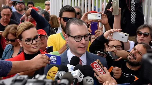 Zanin dando entrevista, com vários microfones e jornalistas ao redor